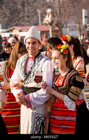 PERNIK, Bulgaria - 26 gennaio 2018: giovane giovani danzatori in bulgaro costumi folcloristici tenere le braccia e ridere la soleggiata giornata invernale all'annuale Int Foto Stock