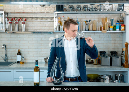 Esperto di vino la valutazione di sapore. Attraente uomo lo scuotimento di un vetro a rendere vorticoso il vino e lo sniffing di sentire ogni nota di bouquet. Cucina interno Foto Stock