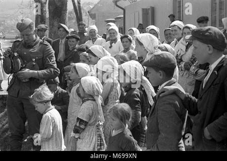 La popolazione locale a guardare i soldati tedeschi di acqua di riempimento di bottiglie in Iugoslavia nell'aprile 1941 durante il WW2 invasione tedesca della Jugoslavia. Foto Stock