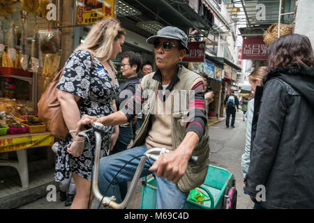 19 Febbraio 2018 - Tai O, l'Isola di Lantau, Hong Kong. Uomini locale del villaggio di pescatori, escursioni in bicicletta attraverso le strette e affollate di turisti strade. Foto Stock