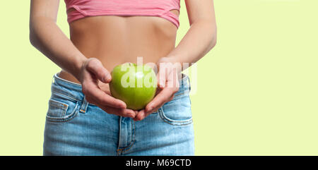 Concetto di dieta. Bella donna perfetta con cintura slim è in possesso di Apple su sbiadito sfondo pastello Foto Stock