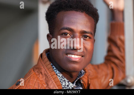 Un bel fiducioso giovane uomo nero in giacca di pelle sorrisi a fotocamera Foto Stock