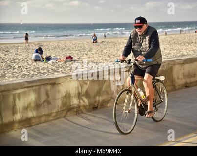 Senior, uomo anziano bicicletta pedalando lungo la popolare spiaggia lastricata boardwalk in Mission Beach, San Diego, California, Stati Uniti d'America Foto Stock
