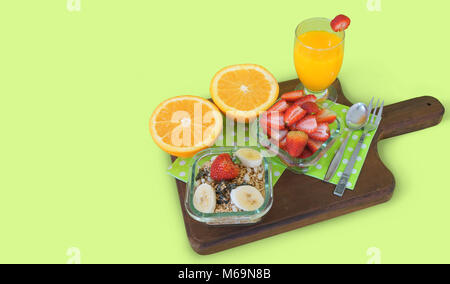 Una sana prima colazione. Vaso di vetro con un trito di fragole, vaso di vetro con granola con pezzi di banana servita con coppa di vetro con succo di arancia Foto Stock