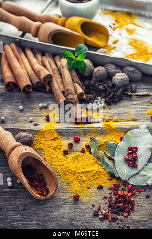 Condire con le spezie in cucchiai di legno sul tavolo in legno in stile rustico.pepe, cannella, chiodi di garofano e menta Foto Stock