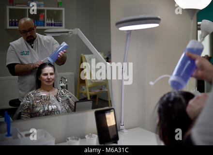 01 marzo 2018, Germania Berlino: Naram Shakra si applica anti pidocchi shampoo alla testa del cliente Monika Beloch al anti pidocchi salon 'Bye bye Laeuse' (lit. bye bye pidocchi). Foto: Britta Pedersen/dpa-Zentralbild/dpa Foto Stock