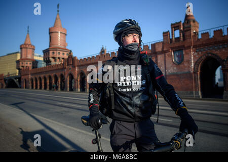 Il 28 febbraio 2018, Germania Berlino : Bike courier Anselmo Holthaus seduto su una moto con un collo sciarpa avvolta intorno a lui sul ponte Oberbaum a Kreuzberg in ghiaccio-basse temperature. A causa della costante meno temperature molti residenti di Berlino sta prendendo il bus e tram anzichè di ciclismo; un opzione che bike corrieri non hanno. Foto: Gregor Fischer/dpa Foto Stock