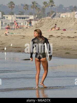 Bella e montare il Latino donna surfer in muta e con tavole da surf sulla spiaggia di Mission Beach, San Diego, California, USA. Foto Stock