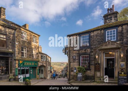 Haworth villaggio dove Bronte suore vissero, vista lungo scoscese, pittoresco, stretta strada principale, Black Bull pub in primo piano - West Yorkshire, Inghilterra, Regno Unito. Foto Stock