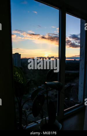 Luminose blu cielo con bianche nuvole rosa al tramonto sopra sagome scure di grandi case di città attraverso il telaio del finestrino Foto Stock