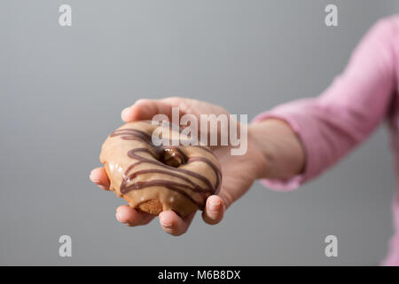 Una mano femminile che offre una ciambella su una perfetta lo sfondo grigio Foto Stock