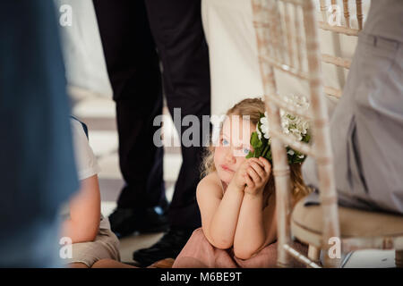 Bambina è seduta sul dancefloor da una tabella a un matrimonio. Ella è guardare la sposa e lo sposo di condividere il loro primo ballo. Foto Stock