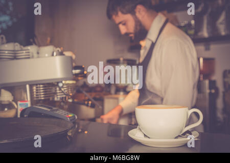 In prossimità della tazza di latte macchiato sul tavolo bar e il barista la preparazione di caffè in background Foto Stock