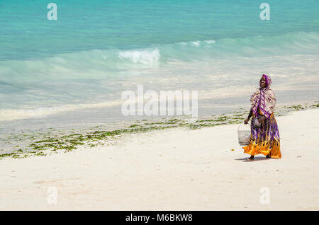 Zanzibar, Tanzania - 4 Dicembre 2014: donna musulmana con abiti colorati a piedi lungo la spiaggia di Nungwi. Foto Stock