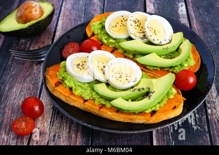 Patate dolci toast con avocado, uova e semi di chia su una piastra di scuro. Tabella scena con uno sfondo di legno. Foto Stock