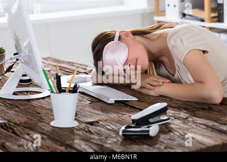 Close-up di giovane donna con Pink Eye Mask di dormire sulla scrivania in ufficio Foto Stock