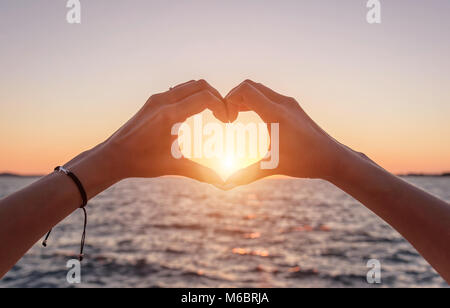Mani in forma di cuore al tramonto e contro lo sfondo del mare. Foto Stock