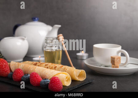 Frittelle di laminati con fresche di fragola e lampone e mirtillo su una pietra nera piastra al buio su un tavolo di pietra con il miele e lo zucchero bianco e co Foto Stock