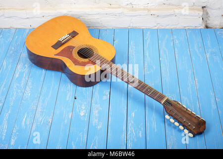 Strumento musicale - Vintage dodici-string chitarra acustica su un mattone di sfondo blu e pavimento in legno. Foto Stock