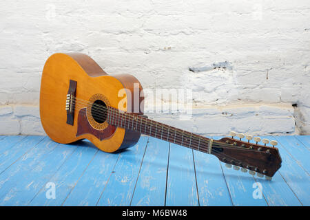 Strumento musicale - Vintage dodici-string chitarra acustica su un mattone di sfondo blu e pavimento in legno. Foto Stock