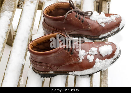 Coperte di neve stivali marrone con lacci legato su una sedia da giardino. Marzo 2018 Foto Stock