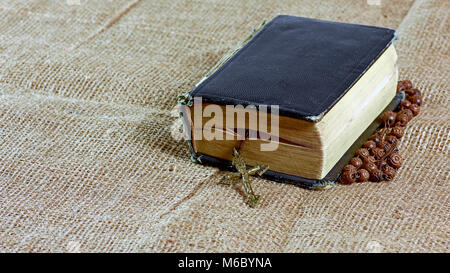 Chiuso un vecchio libro con un rosario in una copertina rigida giacente su un iuta Foto Stock