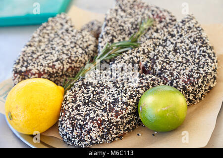 Cuocere le bistecche di tonno in bianco e nero di sesamo su una piastra con lime e limone Foto Stock