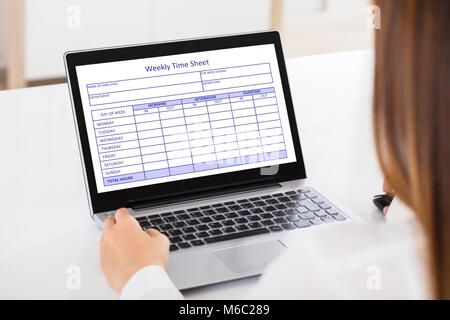 Close-up di una imprenditrice di riempimento tempo settimanale foglio sul computer portatile in ufficio Foto Stock