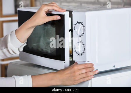 Donna con le mani in mano la chiusura di un forno a microonde porta e preparare il cibo in casa Foto Stock