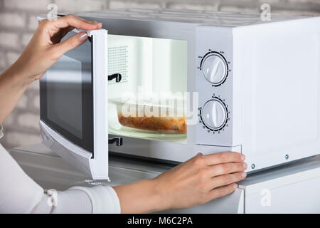 Donna con le mani in mano la chiusura di un forno a microonde porta e preparare il cibo in casa Foto Stock