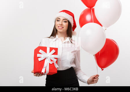 Concetto di natale - giovani caucasici happy business donna con santa hat azienda confezione regalo e palloncino con copia spazio sul lato. Foto Stock