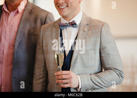 Immagine ravvicinata di un uomo in un vestito con una coppa di champagne mentre si parla di persone a un evento sociale. Foto Stock