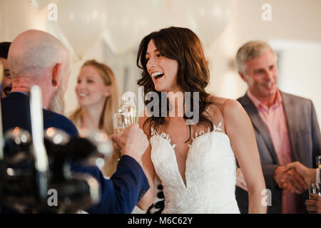 Bella Sposa è socializzare con suo padre e la famiglia il giorno del matrimonio. Essi stanno bevendo champagne e ridere insieme. Foto Stock