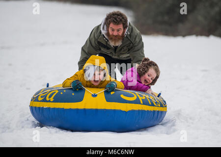 Phil Rogers e bambini Rocco e Ruby sledge utilizzando un gommone in Batheaston nel Somerset dopo la nevicata. Bestia da est, Storm Emma. Foto Stock