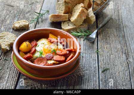Lo spagnolo tapa: salamino piccante Salsiccia con uova fritte e baby patate servita in una terra cotta cazuela piatto Foto Stock