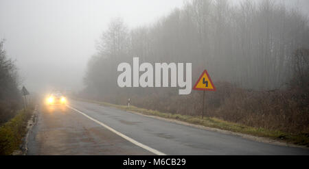 Immagine di una vettura che appare attraverso la nebbia con i fari accesi Foto Stock