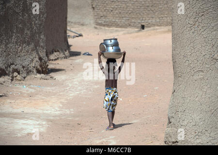 Un giovane, etnica, indigeni Fulani ragazza camminare nel suo villaggio mentre trasportano pentole sul suo capo. Mali, Africa occidentale. Foto Stock