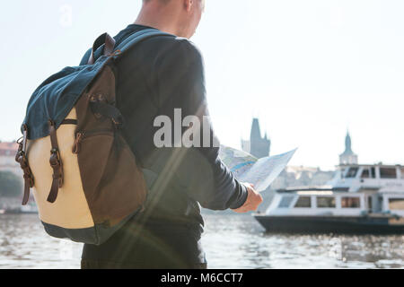 Un giovane uomo turistica con uno zaino in piedi accanto al fiume Moldava a Praga guarda la mappa e ammira l'architettura della città. Charles Bridge è vicino a. Viaggiare in tutta la Repubblica ceca. Foto Stock