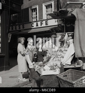 Anni sessanta, storico, Pastore mercato, Mayfair, London, tre onorevoli a un angolo di strada da un open-air di stallo di mercato acquistando frutta e verdura da un commerciante in una mano e il panno cap. Una piccola piazza del XVIII secolo, Shepherd Market si trova tra Piccadilly e Curzon Street e in questa epoca è stata una genuina 'mercato posto' con piccoli negozi e operatori individuali agli angoli delle strade come si vede qui. Foto Stock