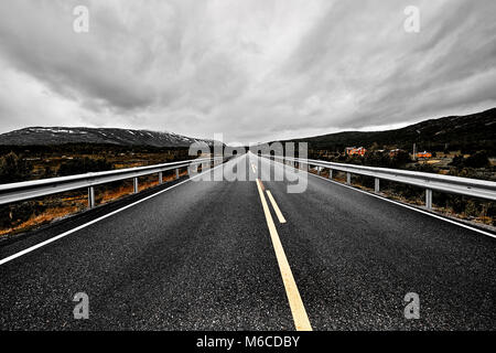 Immagine di una vasta prateria aperta e le montagne con un lastricato highway road che si allunga per quanto l'occhio può vedere con la bellissima natura sotto un cielo nuvoloso Foto Stock