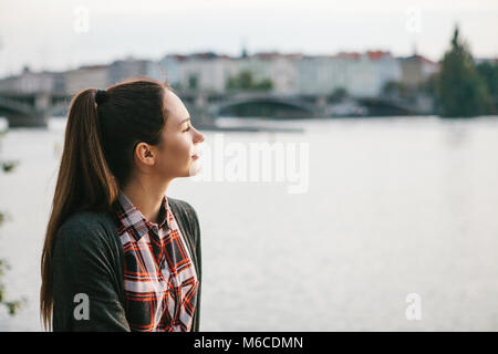 Giovane bella ragazza sulla riva del fiume Moldava a Praga nella Repubblica ceca, ammirando la splendida vista e sognare. Foto Stock