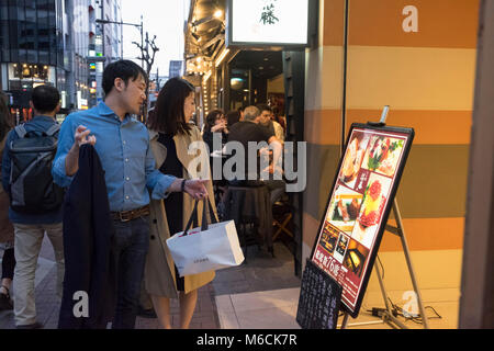 Giovane camminando controllare il menù di un ristorante a Ginza, Tokyo, Giappone Foto Stock