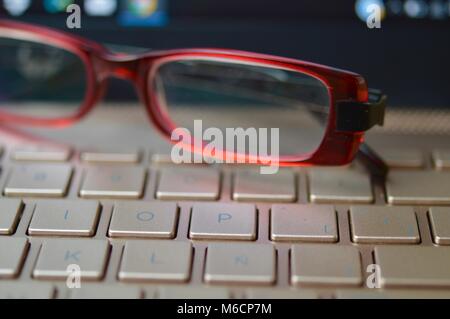 Stanco degli occhiali su un bronzo-colorata tastiera portatile Foto Stock