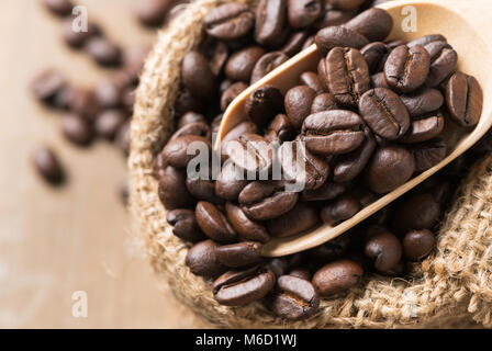 Chiuso di caffè torrefatto in grani in legno scoop su sacco e uno sfondo di legno. Il caffè tradizionale dello sfondo. Foto Stock