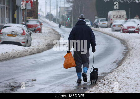 Llantwit Fardre, pontypridd, Wales, Regno Unito - 03 Marzo 2018: Un uomo cammina il suo cane a casa da un negozio lungo un nevoso, viscido street. Veicoli abbandonati parcheggiato sul lato della strada in background. Credito: Elizabeth Foster/Alamy Live News Foto Stock