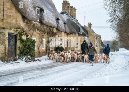 I north cotswolds cacciano i hounds essendo camminati oltre i cottage con tetto di paglia nella neve d'inverno. Broadway, Cotswolds, Worcestershire, Inghilterra Foto Stock