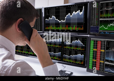 Stock Broker parlando al telefono nella parte anteriore del computer multipli che mostra la schermata dei grafici Foto Stock