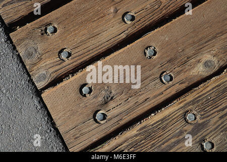 Guardando verso il basso su più weathered sgranate e tavole di legno fissate su un ponte massicciata disposizione diagonale, close-up, due file di bulloni metallici. Foto Stock