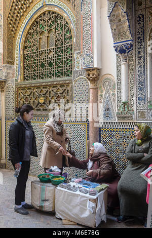 Negozio di incenso e di henna, i clienti e la commessa, sullo sfondo la facciata della Zaouia (Sepolcro) di Moulay Idriss II, la medina di Fez. Il Marocco Foto Stock