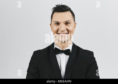 Attraente dai capelli scuri giovane uomo in smoking e farfallino isolata a sfondo bianco. Foto Stock